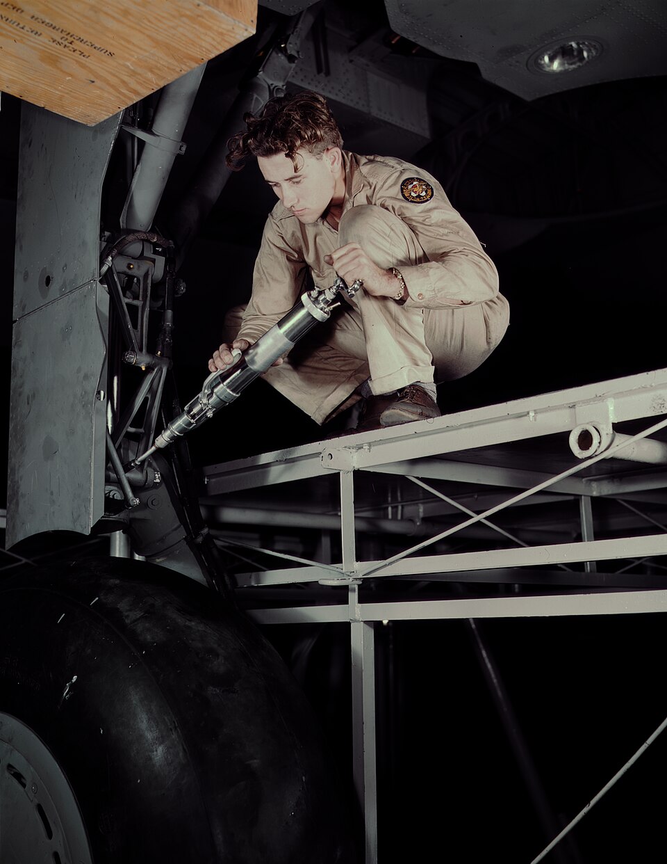Historical photograph of a hydraulic mechanic using a grease gun on an aircraft landing gear